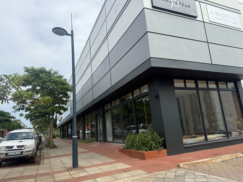 Modern retail storefront featuring large glass display windows, contemporary facade cladding, and a paved pedestrian walkway in a commercial setting.