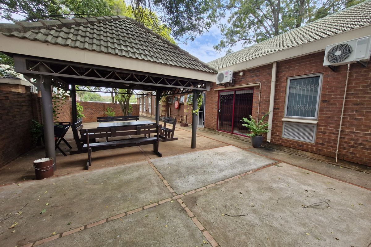 A spacious outdoor patio area featuring a covered gazebo, brick exterior walls, and concrete paving, suitable for office break-out space.