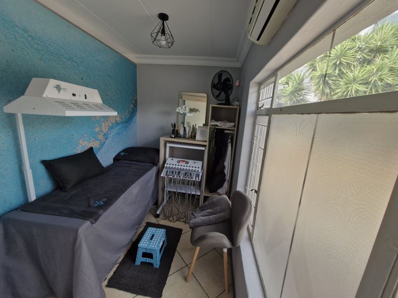 A functional treatment room featuring tiled flooring, a split-system air conditioner, and large windows with security bars, suitable for professional or clinical use.