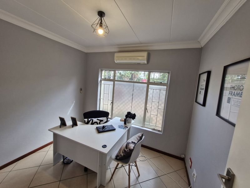 A functional office space featuring tiled flooring, a split-system air conditioner, and a window with security bars, providing a clean and professional work environment.