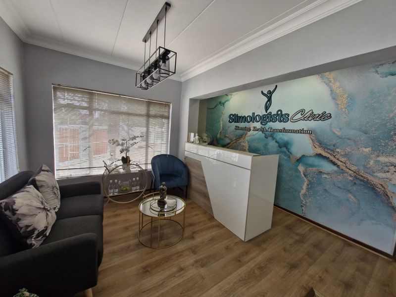 A professional commercial reception area featuring a modern reception desk, wood-look laminate flooring, decorative feature wall, and contemporary pendant lighting.