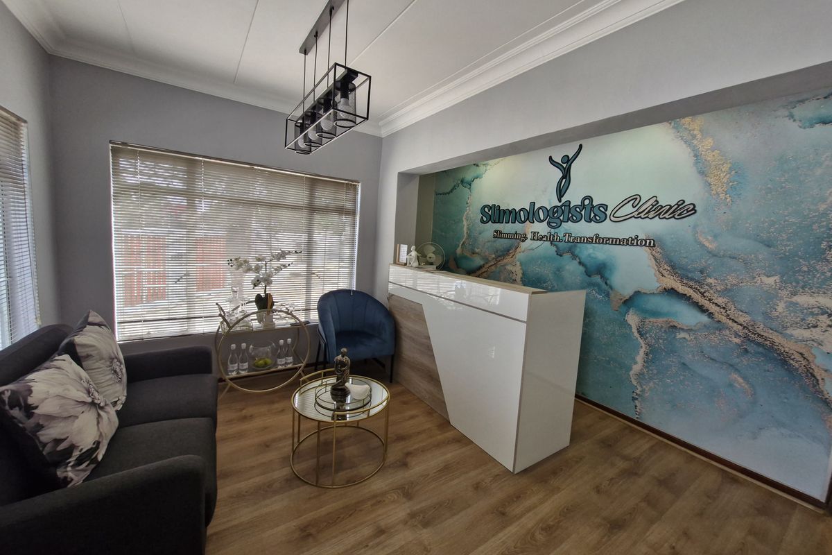A professional commercial reception area featuring a modern reception desk, wood-look laminate flooring, decorative feature wall, and contemporary pendant lighting.