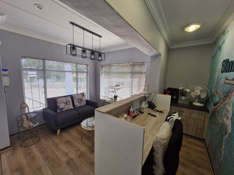 A professional commercial office space featuring a reception desk, built-in cabinetry, laminate flooring, and modern pendant lighting with natural light from large windows.