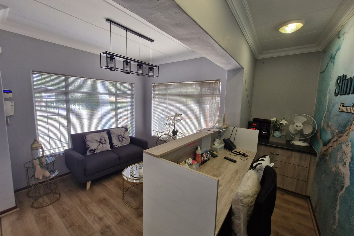 A professional commercial office space featuring a reception desk, built-in cabinetry, laminate flooring, and modern pendant lighting with natural light from large windows.