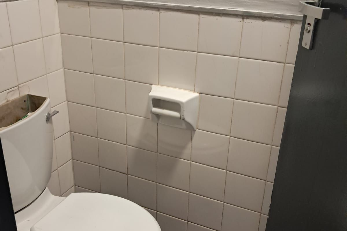 A small office restroom featuring a standard toilet, white wall tiles, and wood-look flooring.