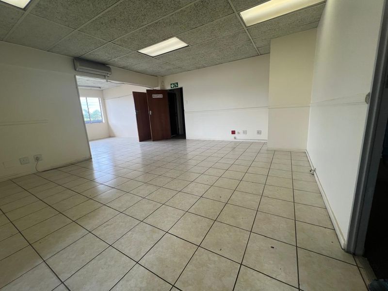 An empty commercial office space featuring ceramic tiled flooring, a suspended ceiling with recessed lighting, and a wall-mounted air conditioning unit.