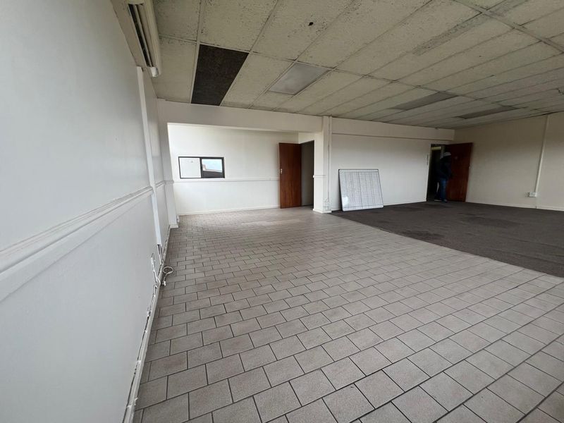 An empty commercial office space featuring a mix of tiled and carpeted flooring, a suspended ceiling, and an integrated air conditioning unit.