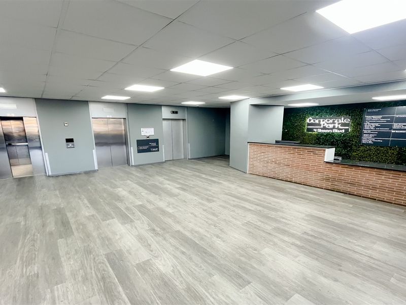 Modern office building lobby featuring a reception desk, multiple elevator access points, and clear directory signage with contemporary finishes.