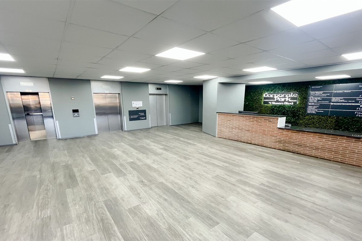 Modern office building lobby featuring a reception desk, multiple elevator access points, and clear directory signage with contemporary finishes.