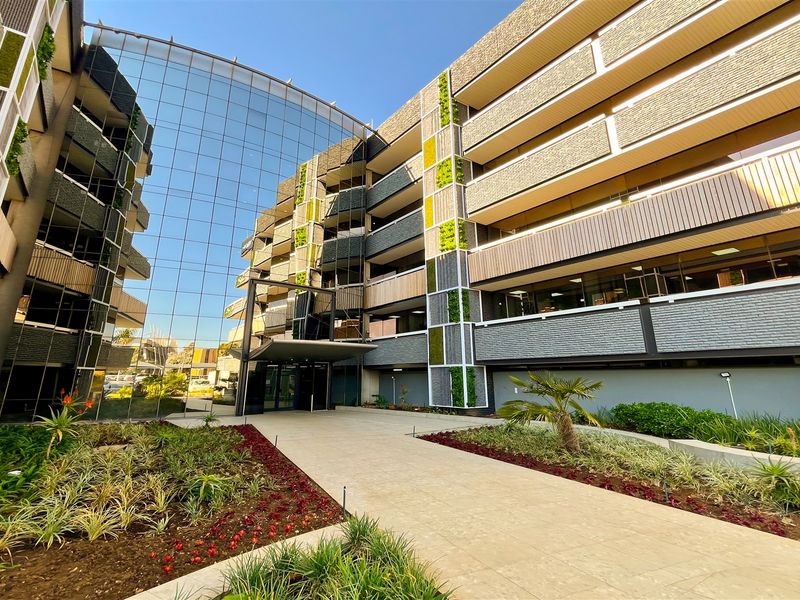 Modern office building exterior featuring a prominent glass curtain wall, vertical garden elements, and a well-maintained paved entrance walkway.