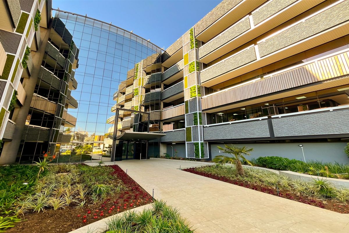 Modern office building exterior featuring a prominent glass curtain wall, vertical garden elements, and a well-maintained paved entrance walkway.
