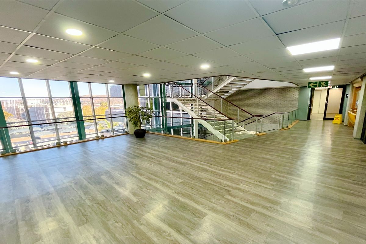 Spacious office building hallway featuring wood-look flooring, a large glass curtain wall with natural light, and an open staircase.