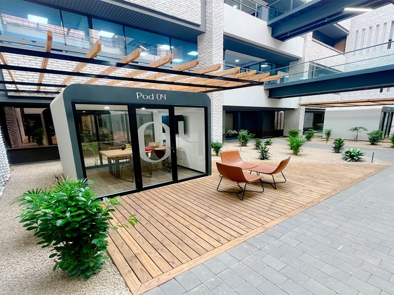 Modern office courtyard featuring a timber deck, pergola, and a glass-walled meeting pod set within a contemporary building complex.