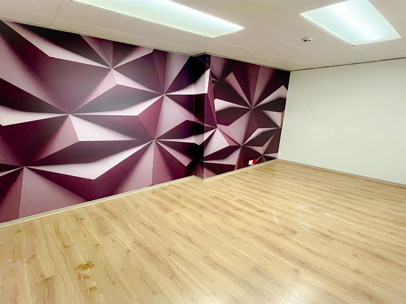 An empty office space featuring light wood-look laminate flooring, a drop ceiling with recessed lighting, and a decorative geometric accent wall.