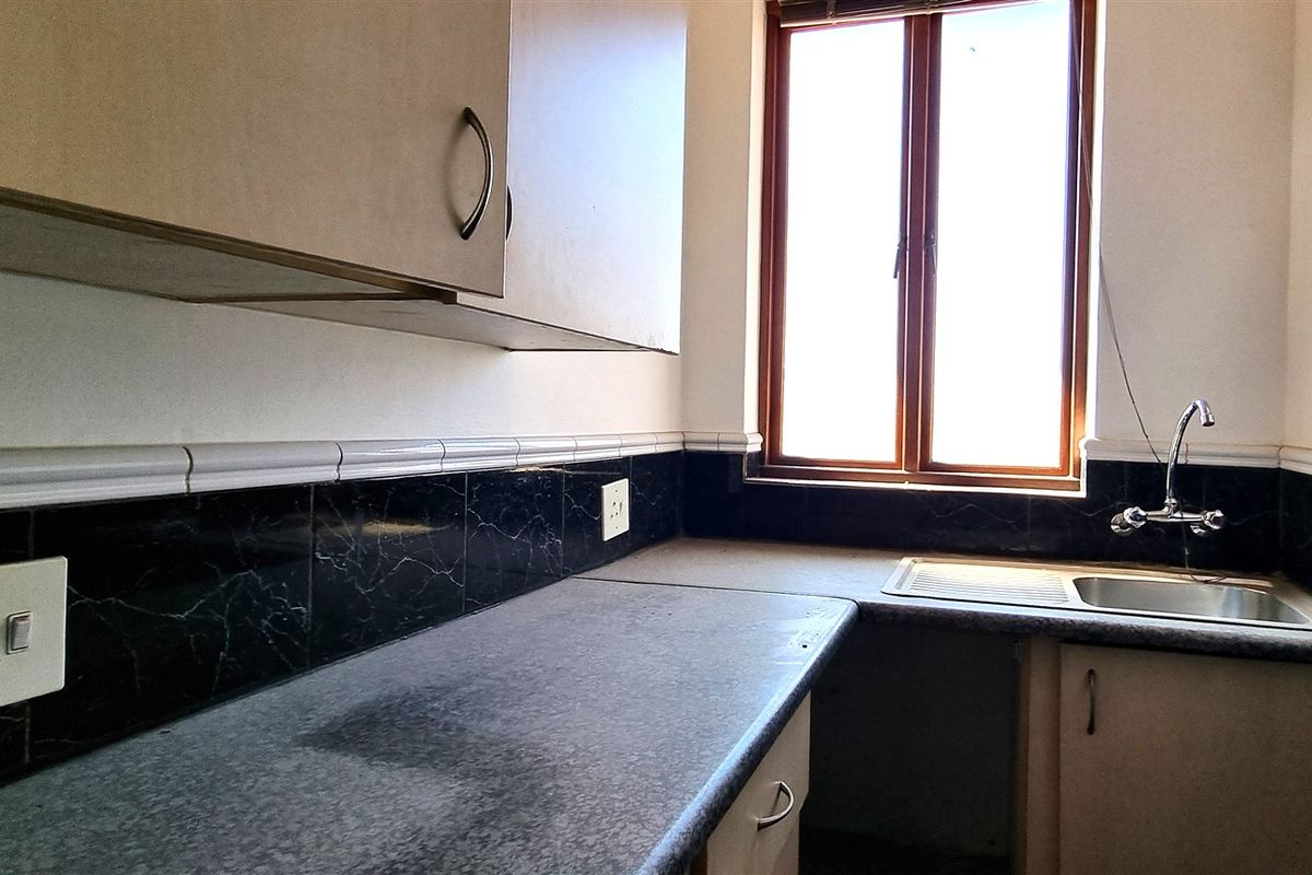 A functional kitchenette area featuring dark marble-effect tiled splashbacks, built-in cabinetry, a stainless steel sink, and a window providing natural light.