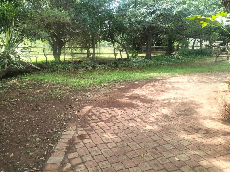 A garden area featuring brick paving, mature trees, and post and rail fencing on a farm property.