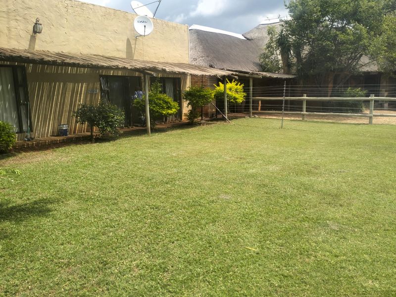 Rear view of the farm property featuring a spacious lawn, a wooden pergola covering the patio area, and traditional thatched roof structures.