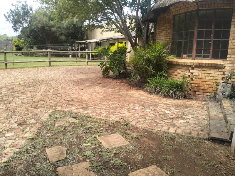 Rear exterior view of a farm-style property featuring brick paving, a thatched roof section, and a timber post and rail fence.
