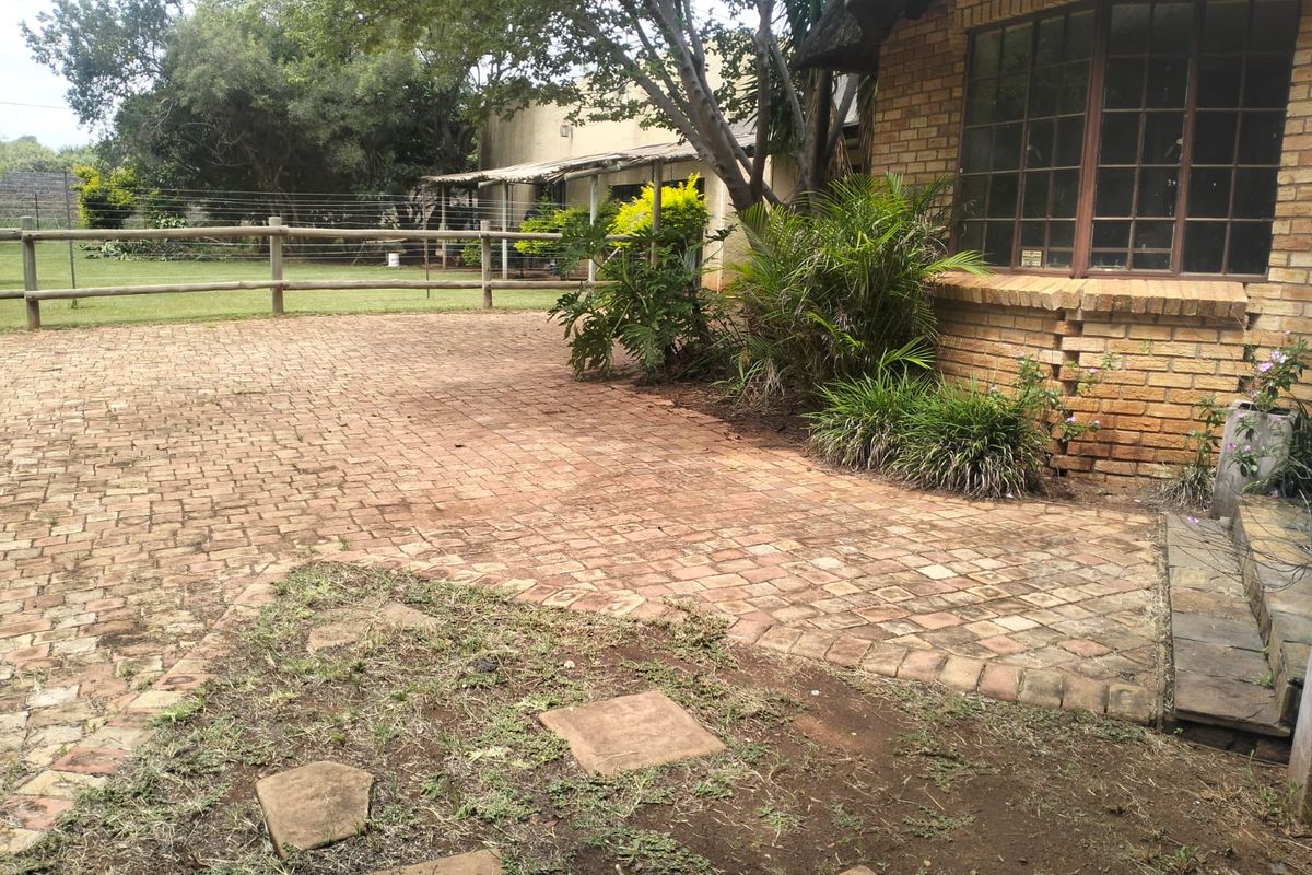Rear exterior view of a farm-style property featuring brick paving, a thatched roof section, and a timber post and rail fence.