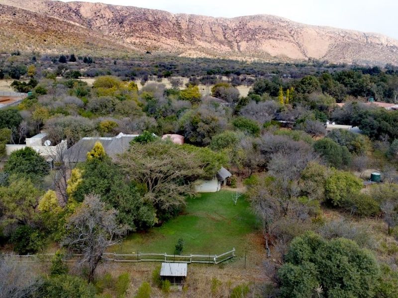 An aerial view of a farm property featuring a dwelling with a thatched roof, surrounded by mature trees and open landscape.