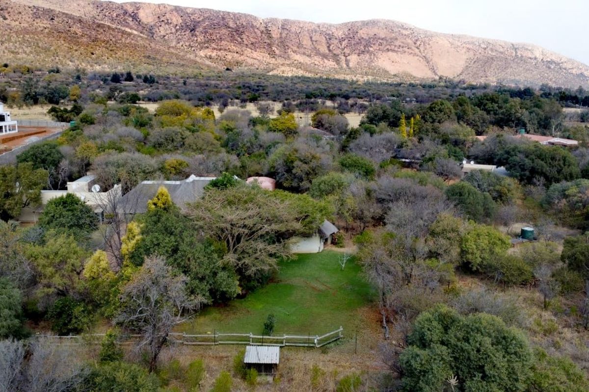 An aerial view of a farm property featuring a dwelling with a thatched roof, surrounded by mature trees and open landscape.