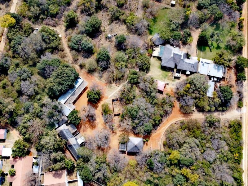 An aerial view of a farm property featuring multiple structures, thatched roofs, extensive mature trees, and a network of gravel access paths.