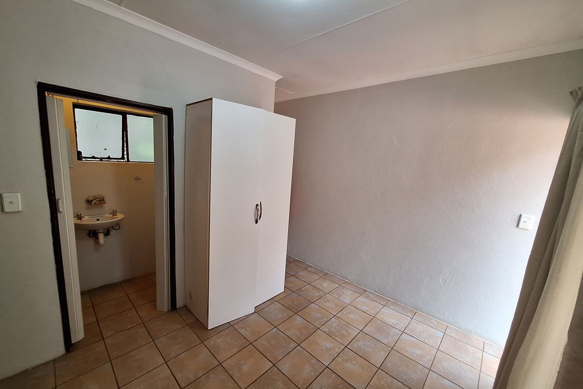 A simple bedroom featuring tiled flooring and an attached en-suite bathroom, offering a functional space ready for personalization.