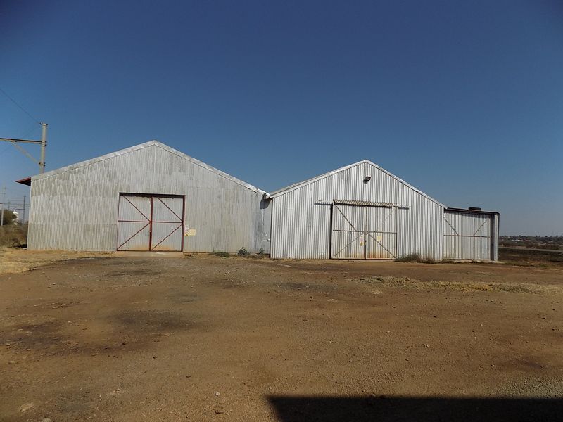 Exterior view of a commercial warehouse facility featuring corrugated metal cladding and large sliding access doors on a dirt lot.