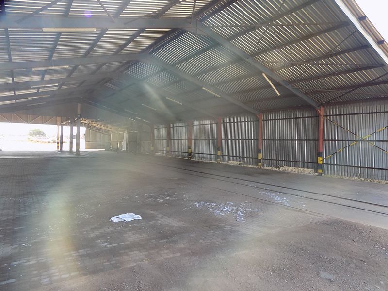 A large, open-plan industrial utility space featuring a high corrugated metal roof, steel frame construction, and durable paved flooring.
