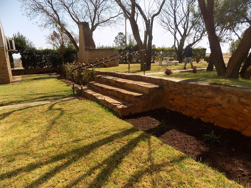 A landscaped garden area featuring stone retaining walls, stone steps with metal handrails, and a brick outdoor chimney structure.