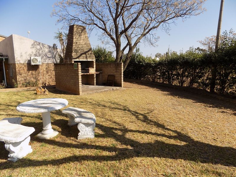 Rear garden area featuring a built-in brick braai, established trees, and a lawn space suitable for outdoor entertainment.