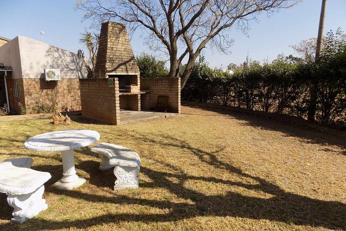 Rear garden area featuring a built-in brick braai, established trees, and a lawn space suitable for outdoor entertainment.