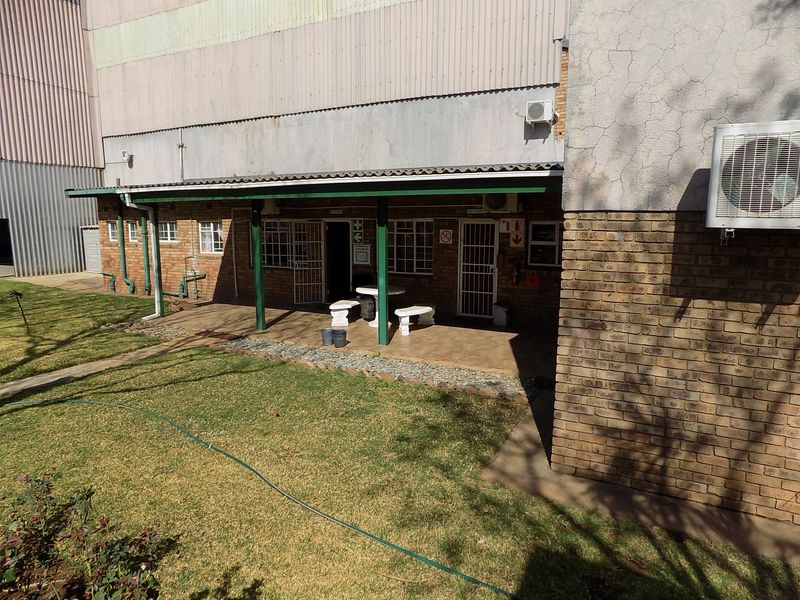 A covered outdoor patio area featuring tiled flooring, security gates, and brick wall construction, adjacent to a lawned garden space.