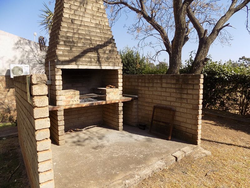 Outdoor entertainment area featuring a traditional built-in brick braai and concrete patio space, set within a garden environment.
