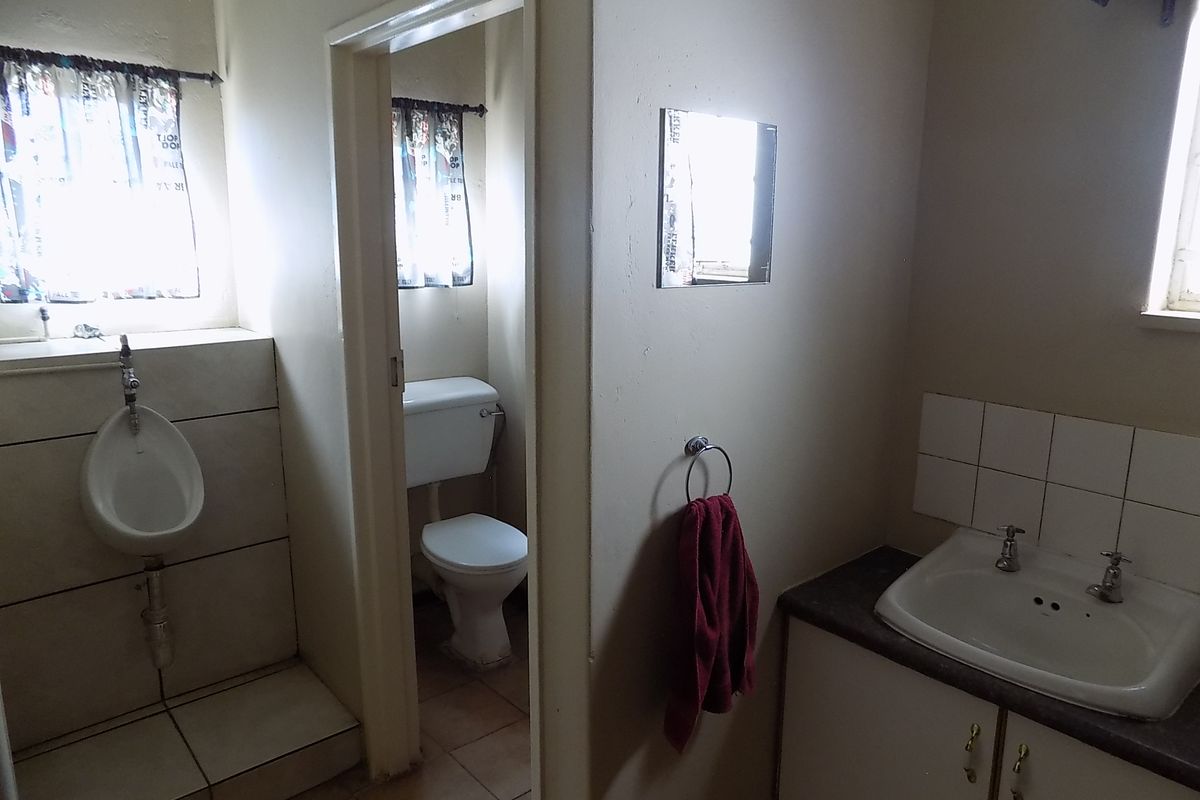 A functional commercial bathroom featuring a wall-mounted urinal, a separate toilet cubicle, and a vanity basin with tiled splashback.