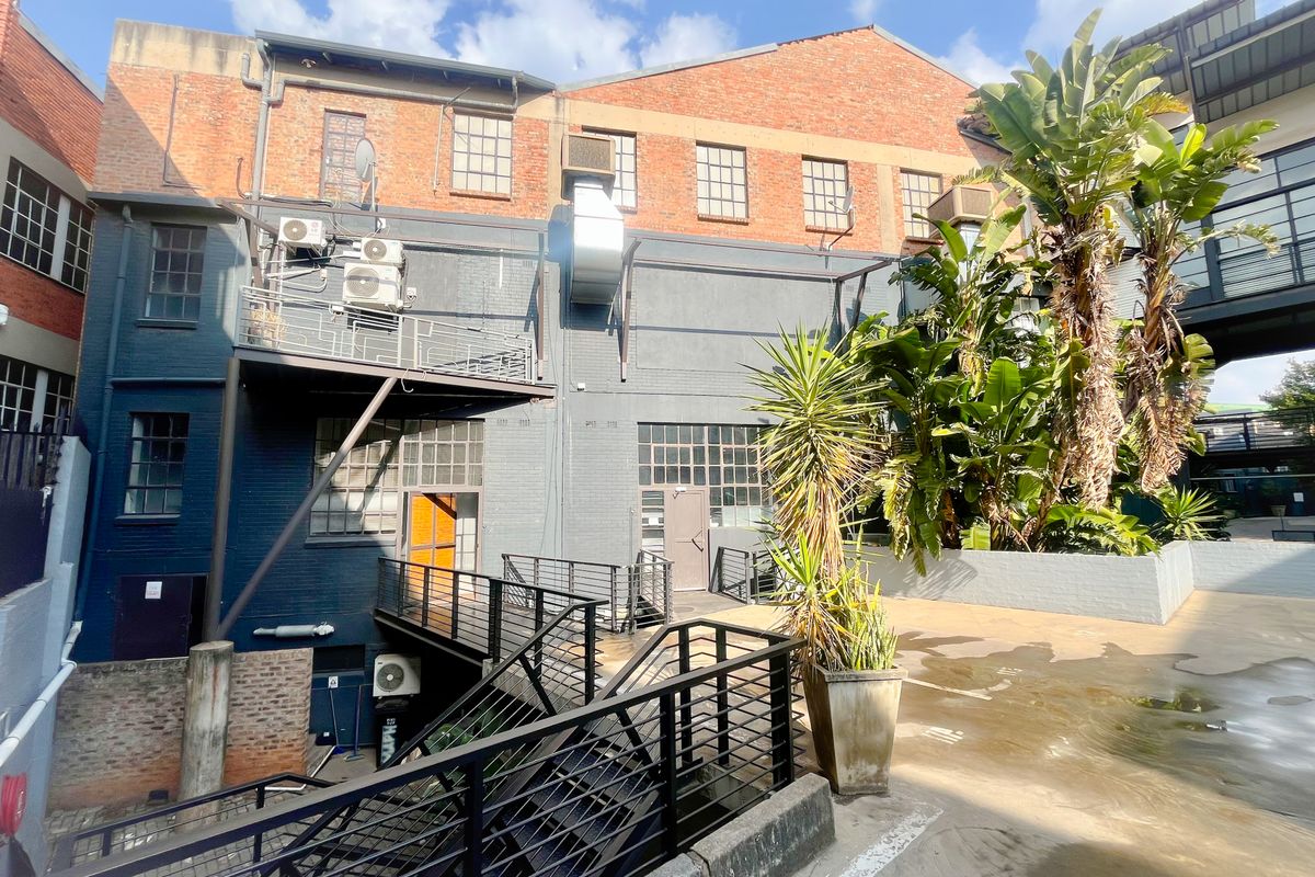 Rear exterior view of a multi-story industrial office building featuring exposed brick, metal staircases, and a paved courtyard area.