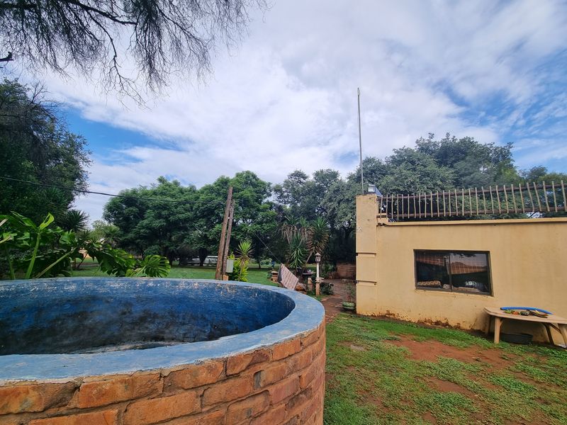 Rear exterior view of the farm property featuring a circular brick water reservoir, perimeter wall with security spikes, and surrounding garden area.