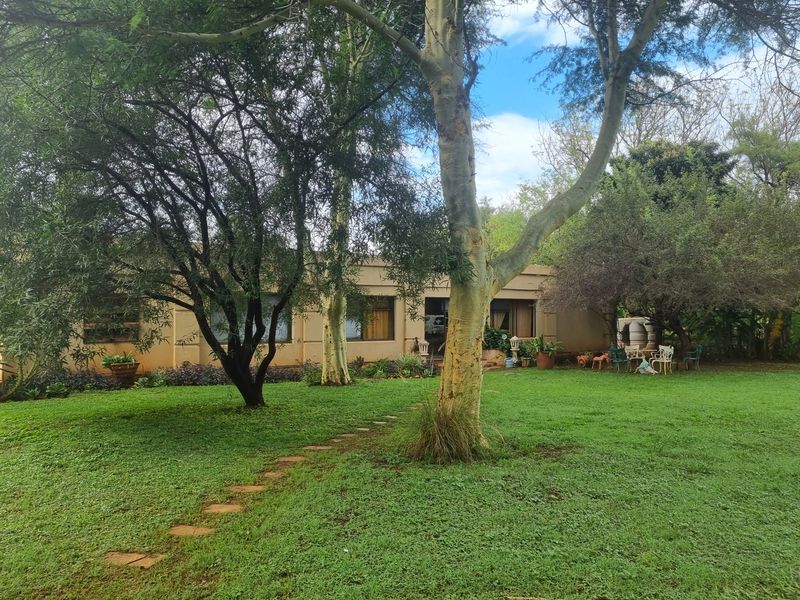 A view of the rear garden featuring a lush lawn, mature trees, a stone pathway, and access to the home via sliding glass doors.
