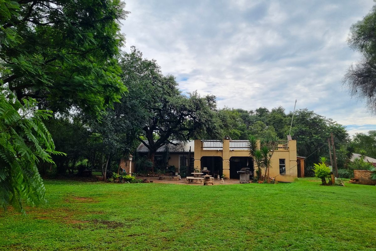 Rear view of the farm property featuring a covered patio, an upper balcony, and extensive garden space with mature trees.