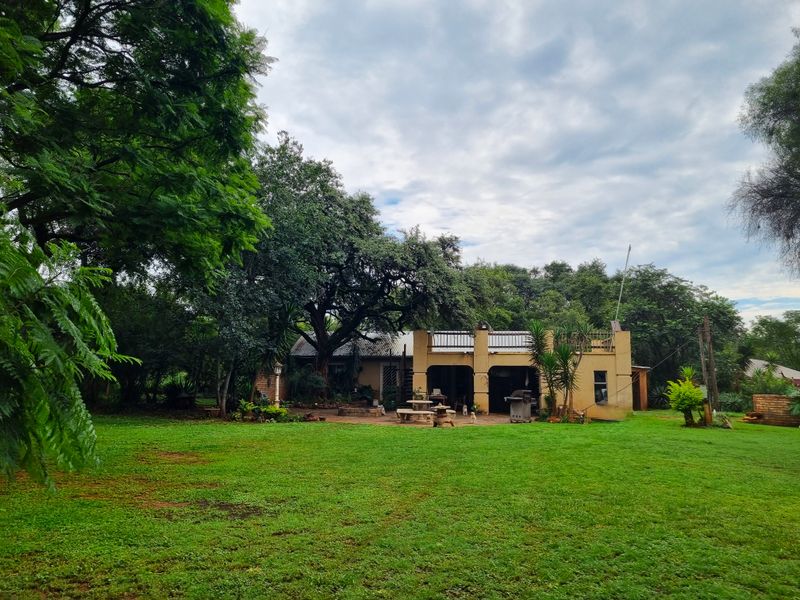 Rear view of the farm property featuring a covered patio, an upper balcony, and extensive garden space with mature trees.