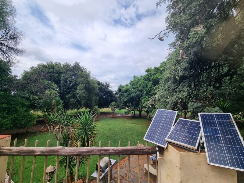 Elevated view overlooking a lush green garden and mature trees, featuring a stone patio area and installed solar panels on the balcony wall.