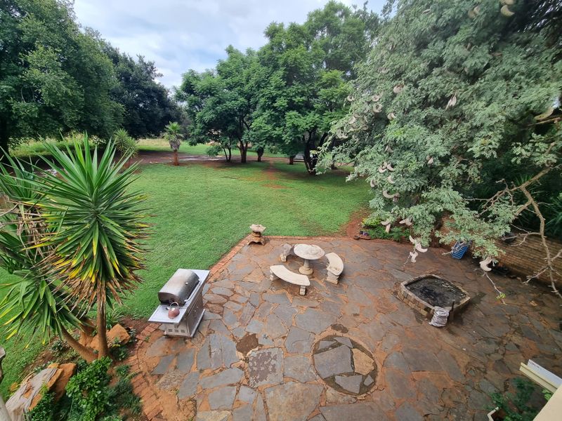 An outdoor patio area featuring natural flagstone paving, a built-in fire pit, and direct access to a spacious, tree-lined garden.