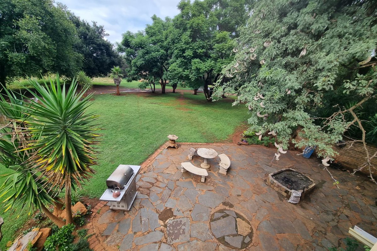 An outdoor patio area featuring natural flagstone paving, a built-in fire pit, and direct access to a spacious, tree-lined garden.