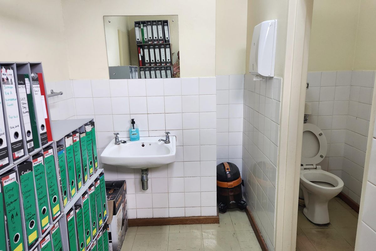 A functional commercial restroom facility featuring a wall-mounted basin, tiled splashbacks, and a private toilet cubicle.