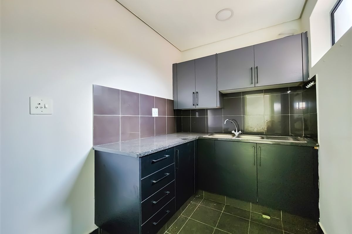 A compact, modern kitchenette featuring dark cabinetry, granite countertops, a stainless steel sink, and tiled finishes, suitable for office utility use.