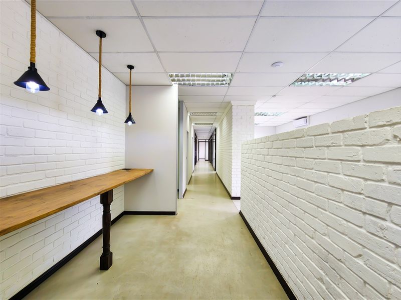 A modern office hallway featuring white painted brick walls, polished concrete floors, a built-in wooden counter, and contemporary pendant lighting.