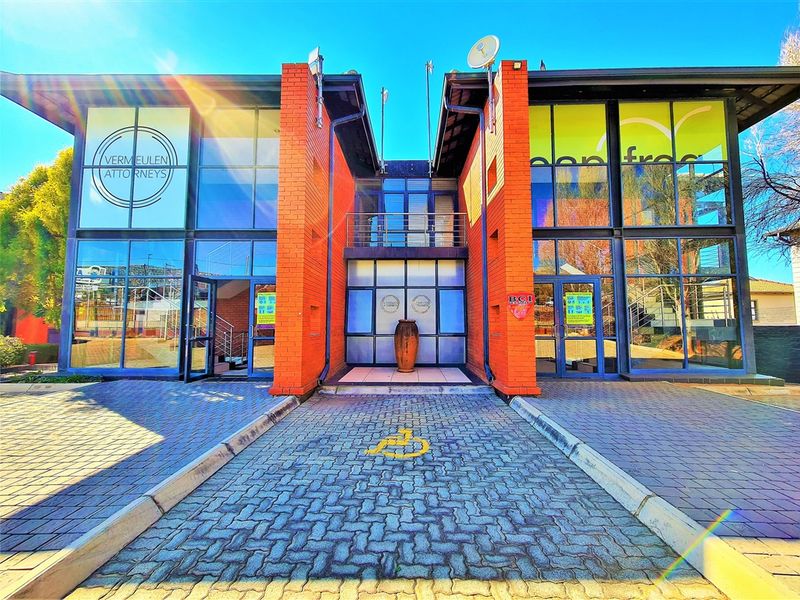 Modern commercial office building featuring a striking brick and glass facade with a paved entrance and designated disabled parking bay.
