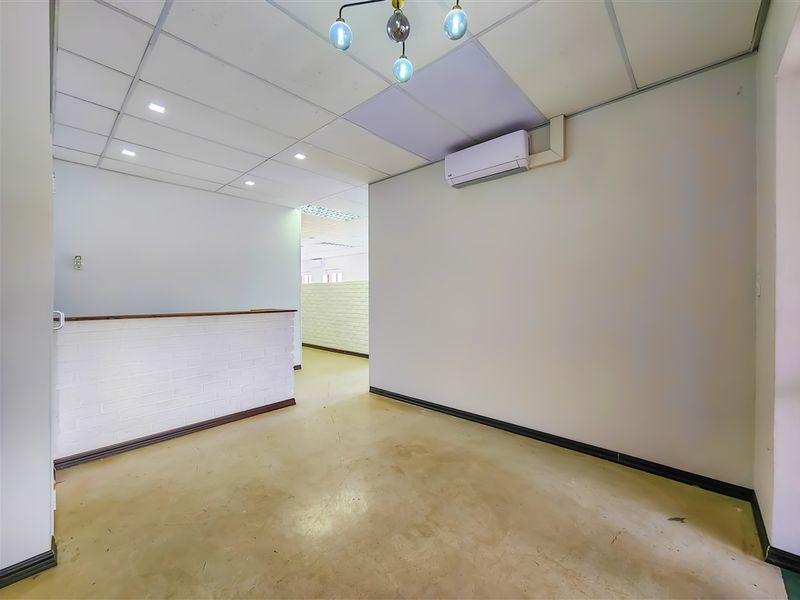 An empty office space featuring a suspended ceiling, split-system air conditioning, and a brick partition wall, suitable for a professional workspace.