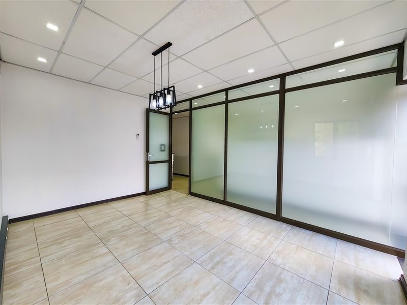 A bright, modern office space featuring tiled flooring, a suspended ceiling with recessed lighting, and professional glass partition walls for a clean, open feel.