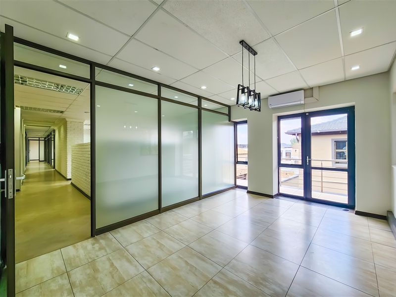 Modern office space featuring glass partition walls, suspended ceiling with recessed lighting, tiled flooring, and direct access to a balcony.